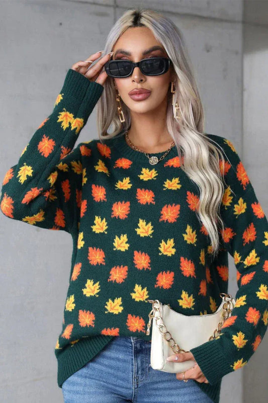 Woman wearing a dark green crew neck sweater with an all-over print of orange and yellow maple leaves. She is also wearing blue jeans, sunglasses, and gold earrings.