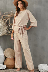 woman posing in a beige wide leg jumpsuit with a tie waist and a hat