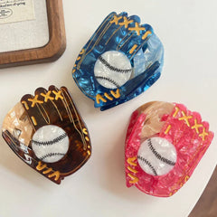 Top-down view of three marbled acrylic baseball glove hair claw clips in blue, brown, and pink