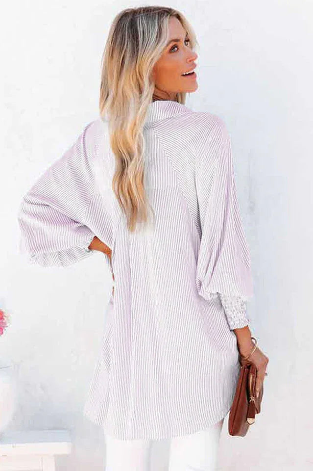Back view of a woman wearing a white and pink pinstripe oversized button-down shirt with billowing sleeves.