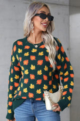 Woman smiling and wearing a dark green sweater with an autumn leaf print. She is holding a white purse with a gold chain strap.
