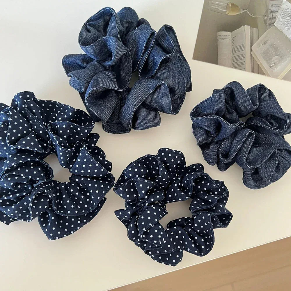 A collection of four scrunchies, two with polka dots and two in denim fabric, arranged on a white surface