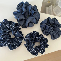 A collection of four scrunchies, two with polka dots and two in denim fabric, arranged on a white surface