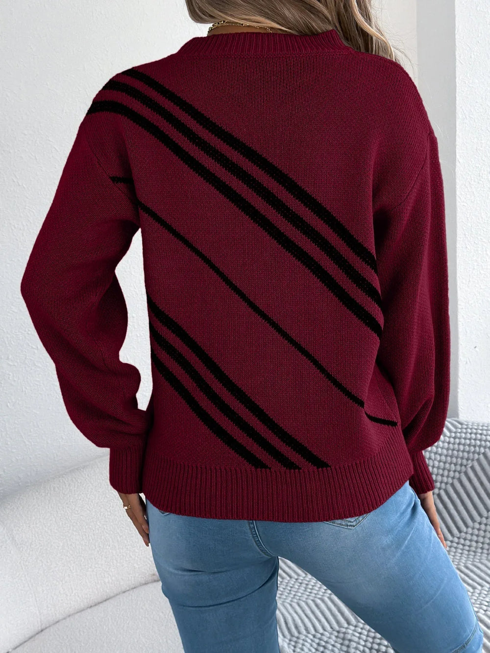 Back view of a woman wearing a burgundy knit sweater with black diagonal stripes, blue jeans.