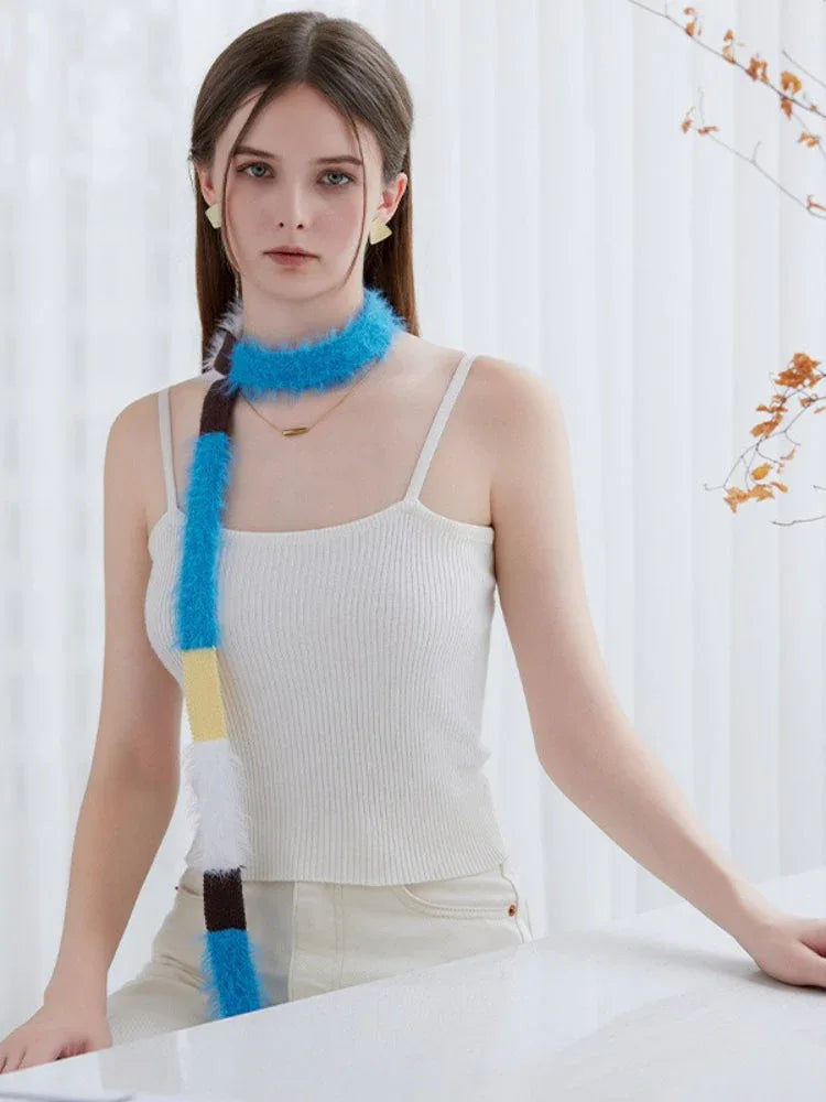 Close-up of a model wearing a white ribbed tank top and off-white pants, with a fluffy, color-blocked scarf draped around her neck.