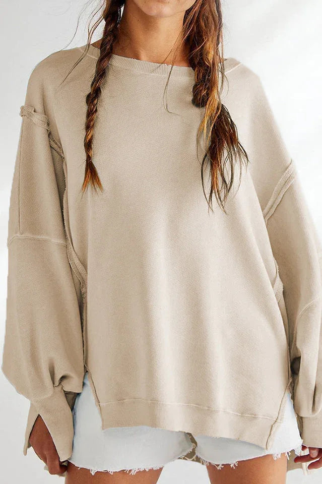 Close-up of a model wearing a tan oversized sweatshirt with a dropped shoulder and distressed hem.