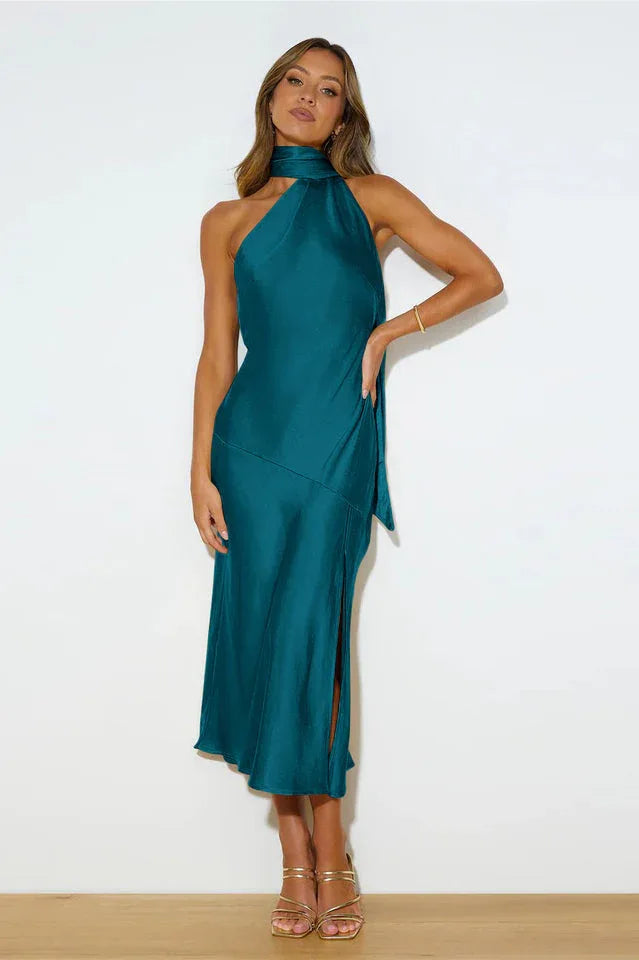 Woman wearing a teal satin halter midi dress with a high slit and tie detail.