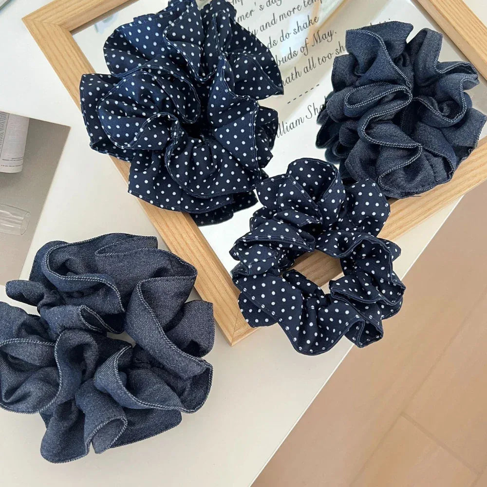 A group of four scrunchies, featuring polka dots and denim textures, displayed on a surface with a mirror reflection