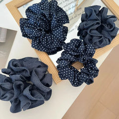 A group of four scrunchies, featuring polka dots and denim textures, displayed on a surface with a mirror reflection