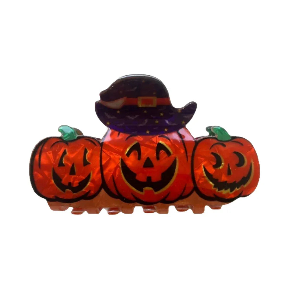 A hair clip featuring three carved pumpkins wearing a witch hat.