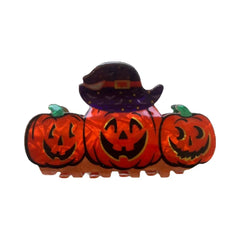 A hair clip featuring three carved pumpkins wearing a witch hat.