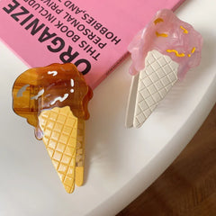 Two ice cream cone hair clips, one pink and one brown, on a white surface with a pink book in the background