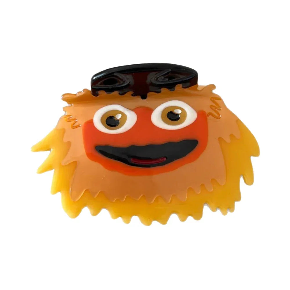 Close-up of a fuzzy orange and yellow character hair clip with large eyes and a black hat.