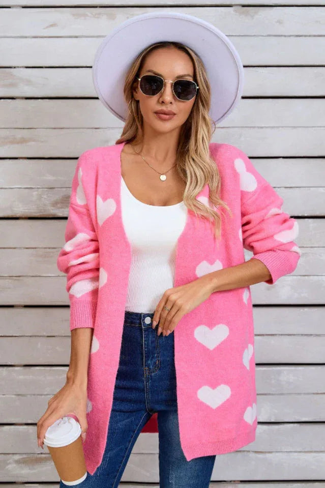 Woman wearing a pink longline cardigan with a white heart print, a white tank top, and blue jeans, holding a coffee cup.