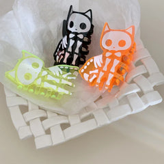 Three skeleton cat claw hair clips in black, orange, and neon green