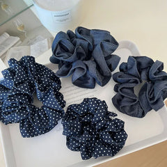 Four scrunchies, including polka dot and denim styles, placed on a white tray next to decorative items