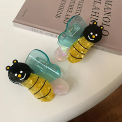 A pair of bee-shaped hair clips with blue wings, displayed on a book.