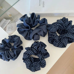 An overhead view of four scrunchies, two polka dot and two denim, arranged on a white surface with books in the background