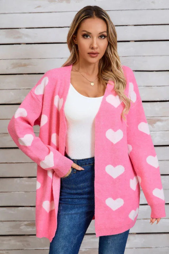 Woman wearing a pink longline cardigan with a white heart print, a white tank top, and blue jeans.