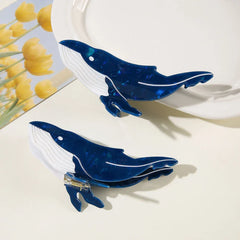 Two blue and white whale-shaped hair claw clips on a white surface, with one slightly elevated.