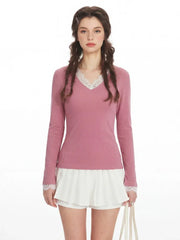Woman wearing a pink long-sleeved top with white lace trim at the neckline and cuffs, and white pleated shorts.