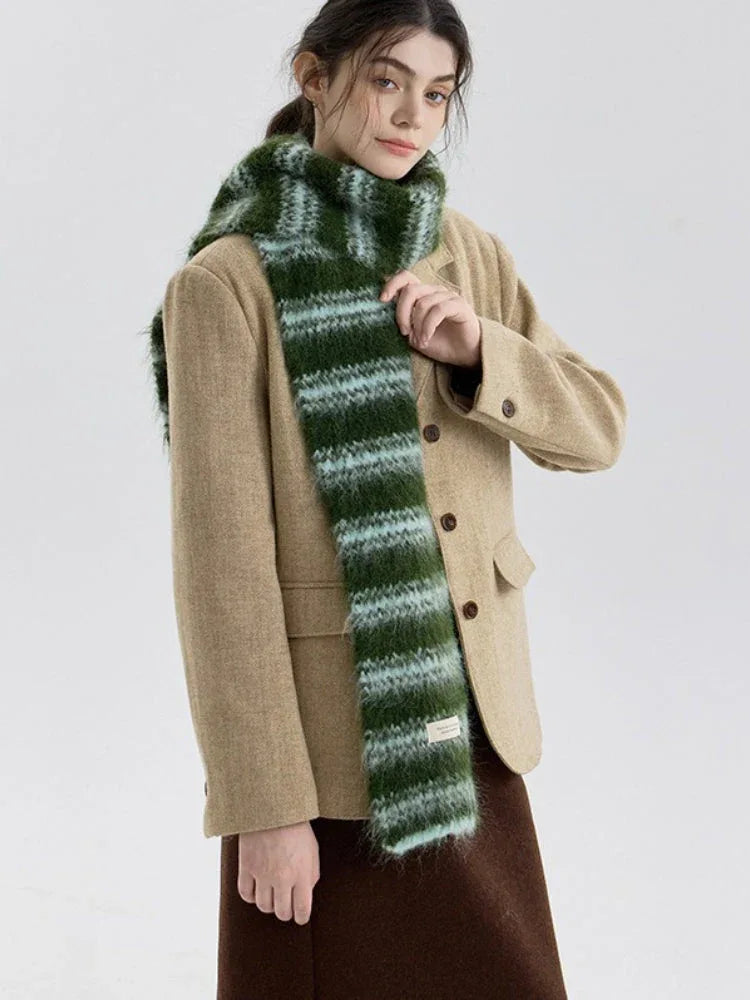 Model adjusting a green and blue striped scarf while wearing a tan blazer and a brown skirt.