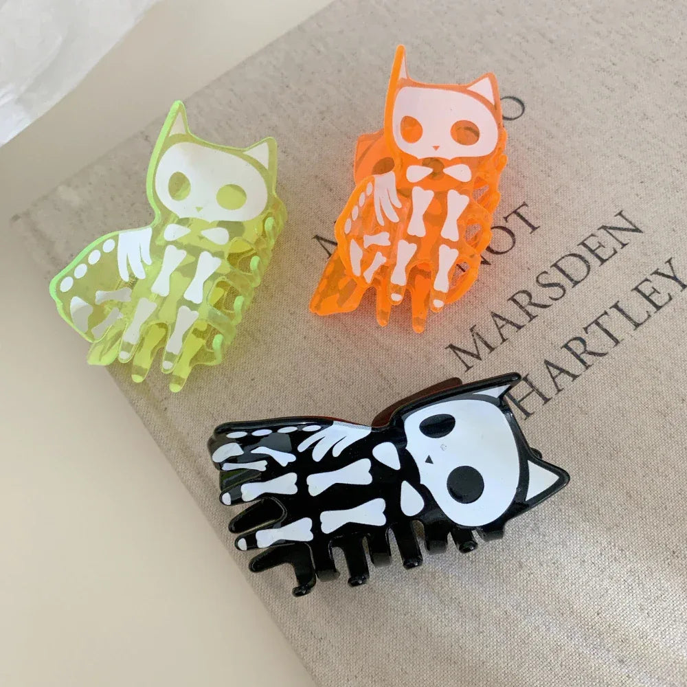 Three skeleton cat claw hair clips in black, orange, and neon green on a book