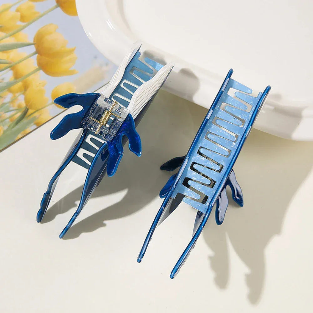 The underside view of two blue and white whale-shaped hair claw clips, showing the internal mechanism.
