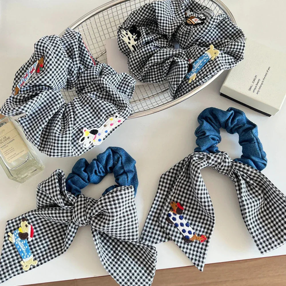Assortment of black and white gingham scrunchies with denim bows and dog appliques on a white surface