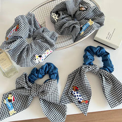 Assortment of black and white gingham scrunchies with denim bows and dog appliques on a white surface