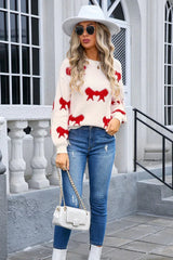 Woman wearing a cream knit sweater with a red bow pattern, blue jeans, and a white handbag