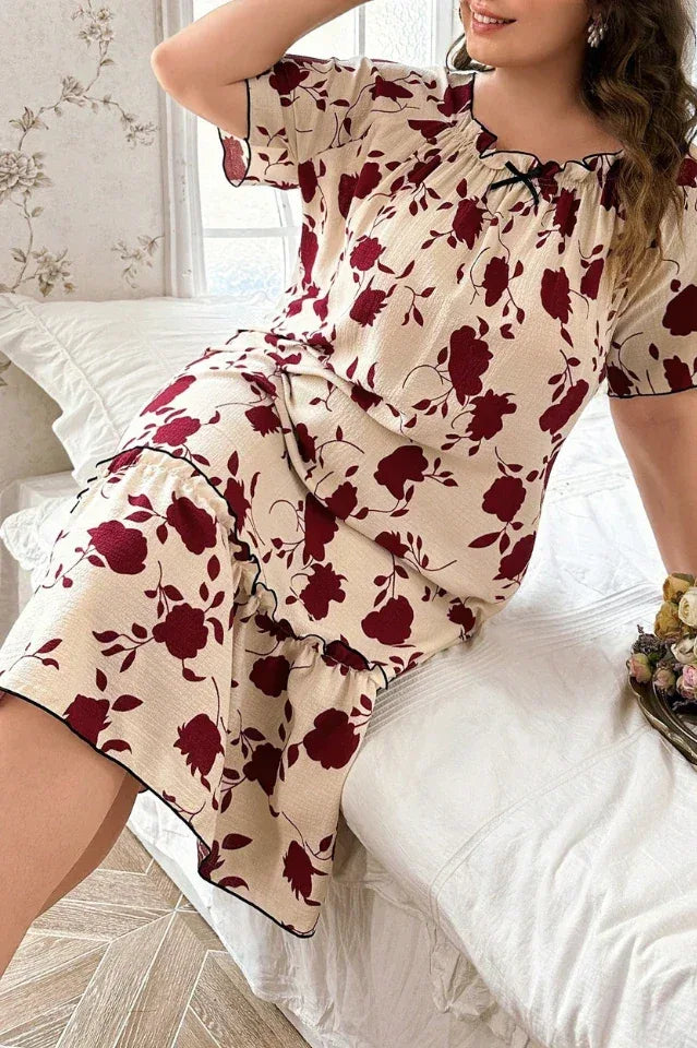Plus size woman in a cream and red floral print short sleeve ruffled hem nightgown sitting on a bed.