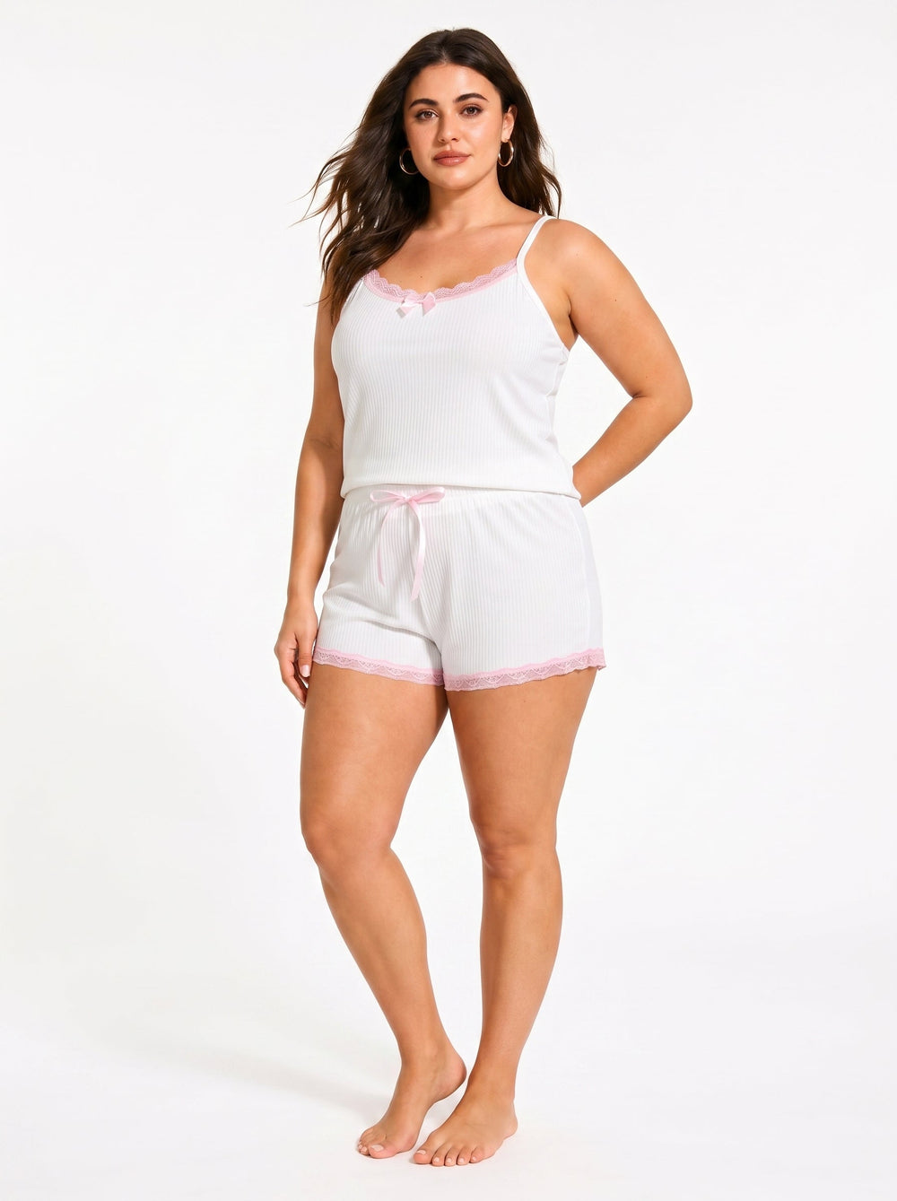 Woman standing with hands behind back in a white ribbed camisole and shorts pajama set with pink lace trim.