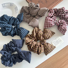 Several plaid scrunchies with bow details are displayed on a white tabletop, some partially in a tray.
