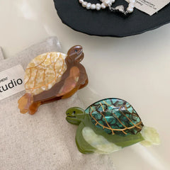 Overhead view of two acetate turtle hair clips, one green and one brown/tan, on a textured fabric