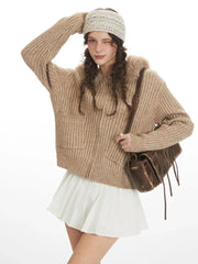 Close-up of a model wearing a beige ribbed knit hooded jacket with faux fur trim, winking and touching her hair.