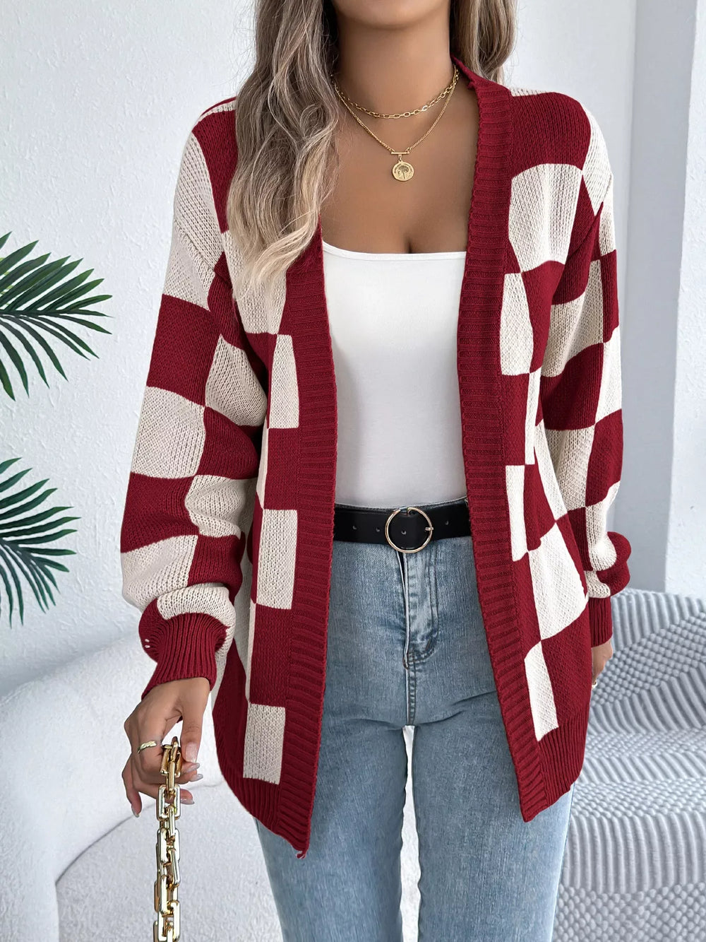 Woman in a red and cream checkerboard knit cardigan and blue jeans, with a white quilted handbag.