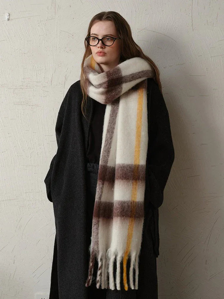 Woman wearing a long dark coat and a large plaid scarf with white, brown, and yellow stripes, with the scarf draped around her neck.
