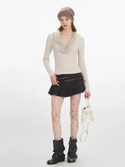 Woman wearing a cream long-sleeve top with fur trim, a black pleated mini skirt, decorative tights, and black boots, holding a white bucket bag, front view.