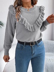 woman wearing a grey knit sweater with ruffle trim, blue jeans, and a black belt from the front