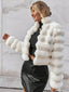 Woman wearing a white faux fur cropped jacket over a black top and black skirt, smiling outdoors.