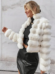 Woman wearing a white faux fur cropped jacket over a black top and black skirt, smiling outdoors.
