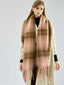 Woman in a cream coat with a large, soft plaid scarf in pink and brown draped around her neck.