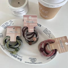 A collection of spiral hair ties on a decorative plate with text.