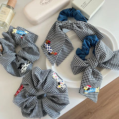 Close-up of black and white gingham scrunchies with denim bows, showcasing embroidered dog designs