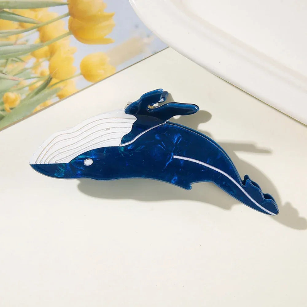 A close-up of a blue and white whale-shaped hair claw clip on a white surface.