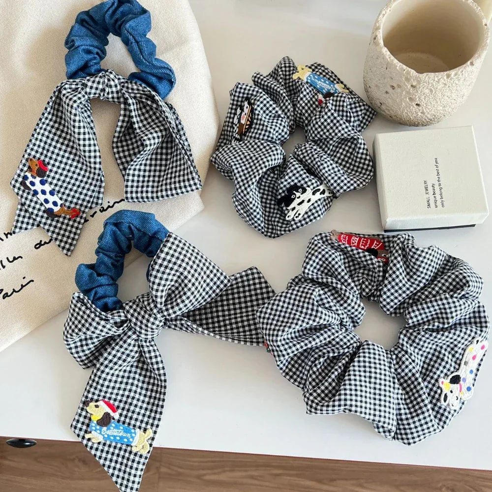 Arrangement of black and white gingham scrunchies with denim and embroidered dog details, styled on a table