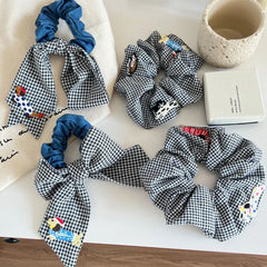 Arrangement of black and white gingham scrunchies with denim and embroidered dog details, styled on a table