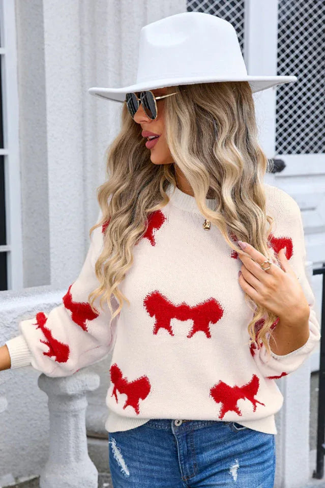 Woman wearing a cream knit sweater with a red bow pattern, white hat, and sunglasses