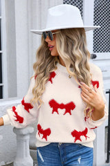 Woman wearing a cream knit sweater with a red bow pattern, white hat, and sunglasses